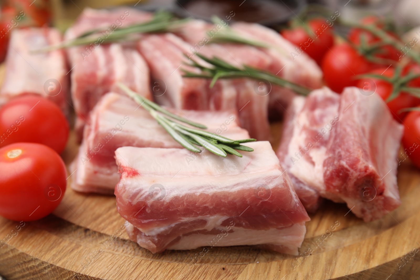 Photo of Cut raw pork ribs with rosemary and tomatoes on wooden board, closeup