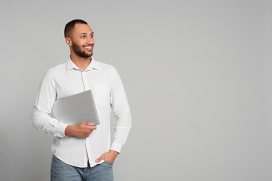 Photo of Smiling young man with laptop on grey background, space for text