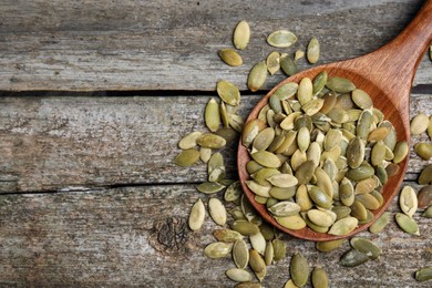Photo of Spoon with pumpkin seeds on wooden table, flat lay. Space for text