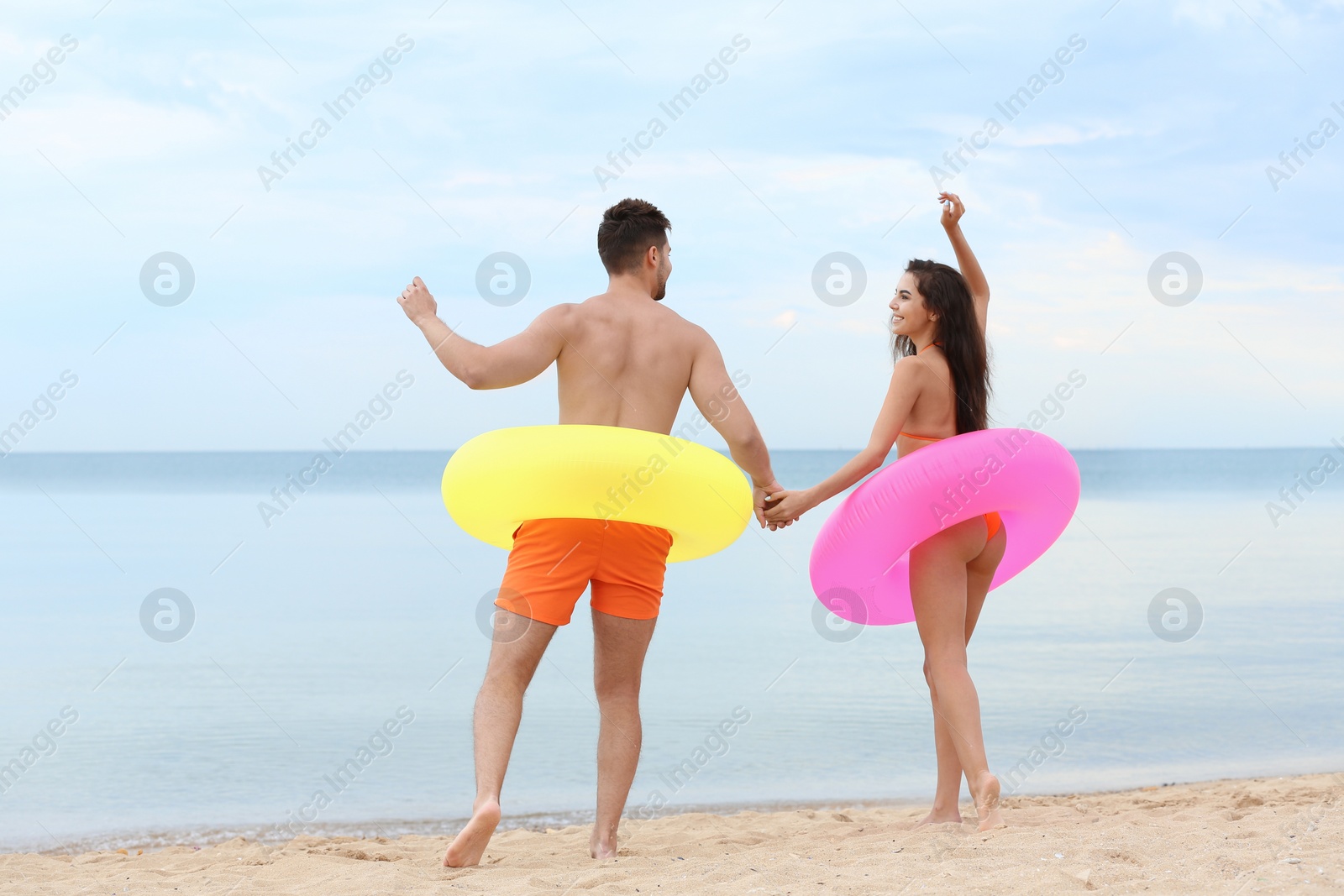 Photo of Happy young couple having fun with inflatable rings on beach near sea