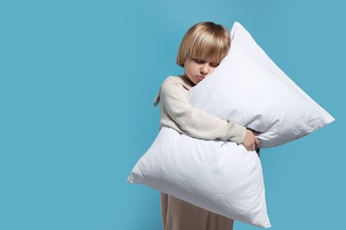 Boy in pajamas hugging pillow on light blue background, space for text