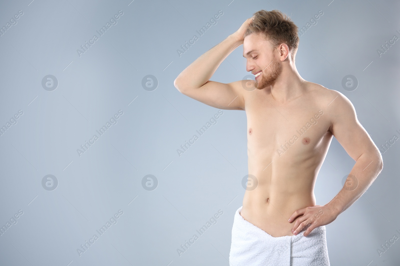 Photo of Portrait of young man with slim body in towel on grey background. Space for text