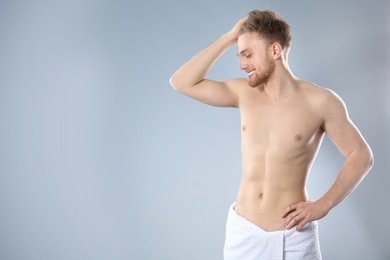 Portrait of young man with slim body in towel on grey background. Space for text