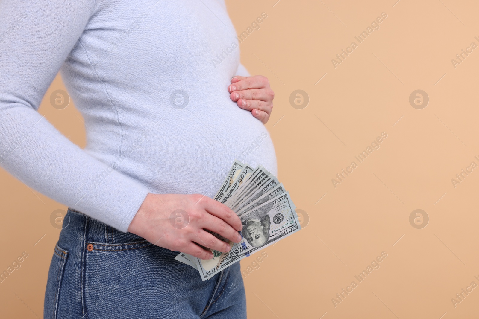 Photo of Surrogate mother. Pregnant woman with dollar banknotes on beige background, closeup. Space for text