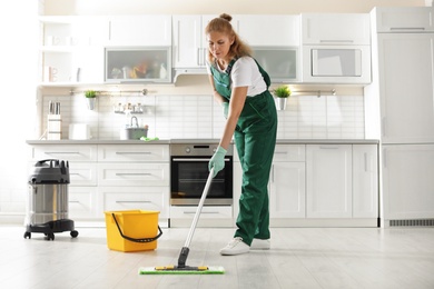 Professional janitor cleaning floor with mop in kitchen