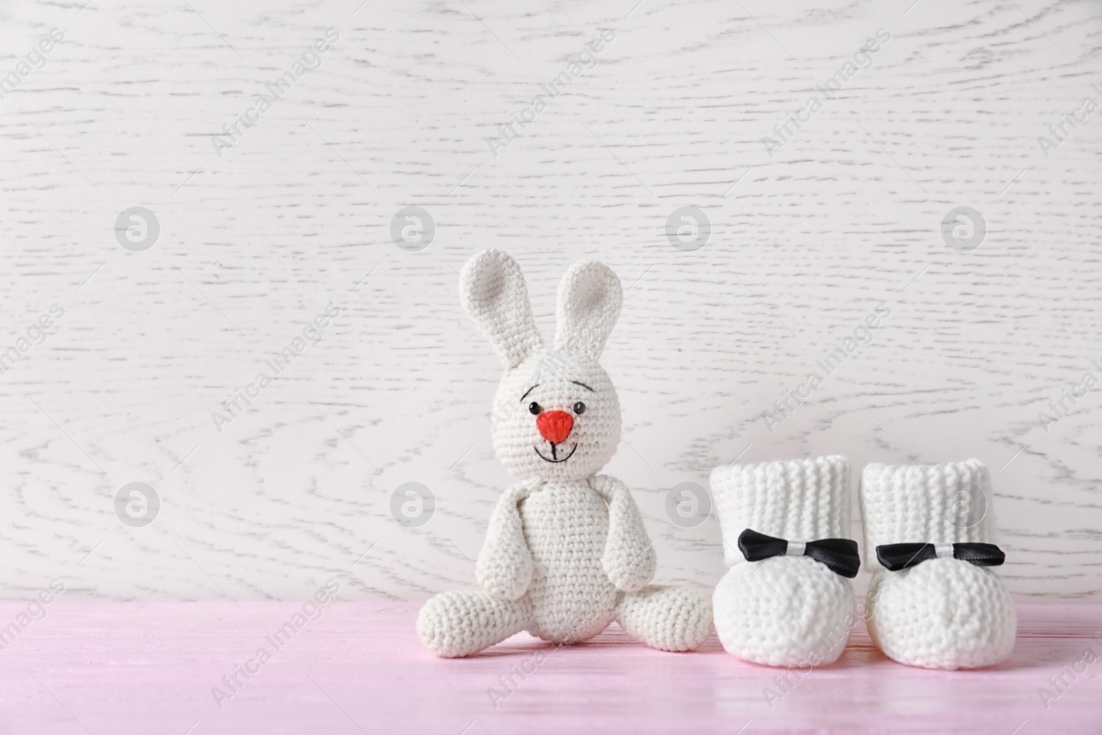 Photo of Handmade baby booties and stuffed rabbit on table against wooden background
