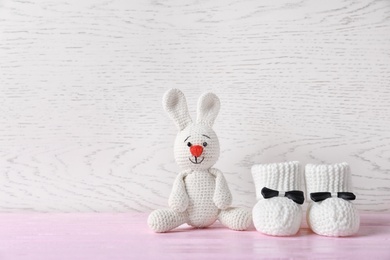 Handmade baby booties and stuffed rabbit on table against wooden background