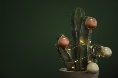 Beautiful cactus with Christmas balls and festive lights  on green background, closeup. Space for text