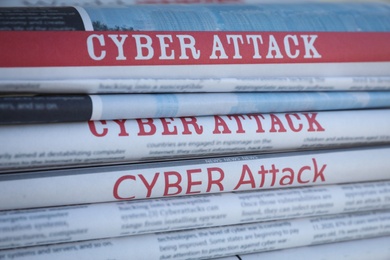 Photo of Stacked newspapers with headlines CYBER ATTACK as background, closeup