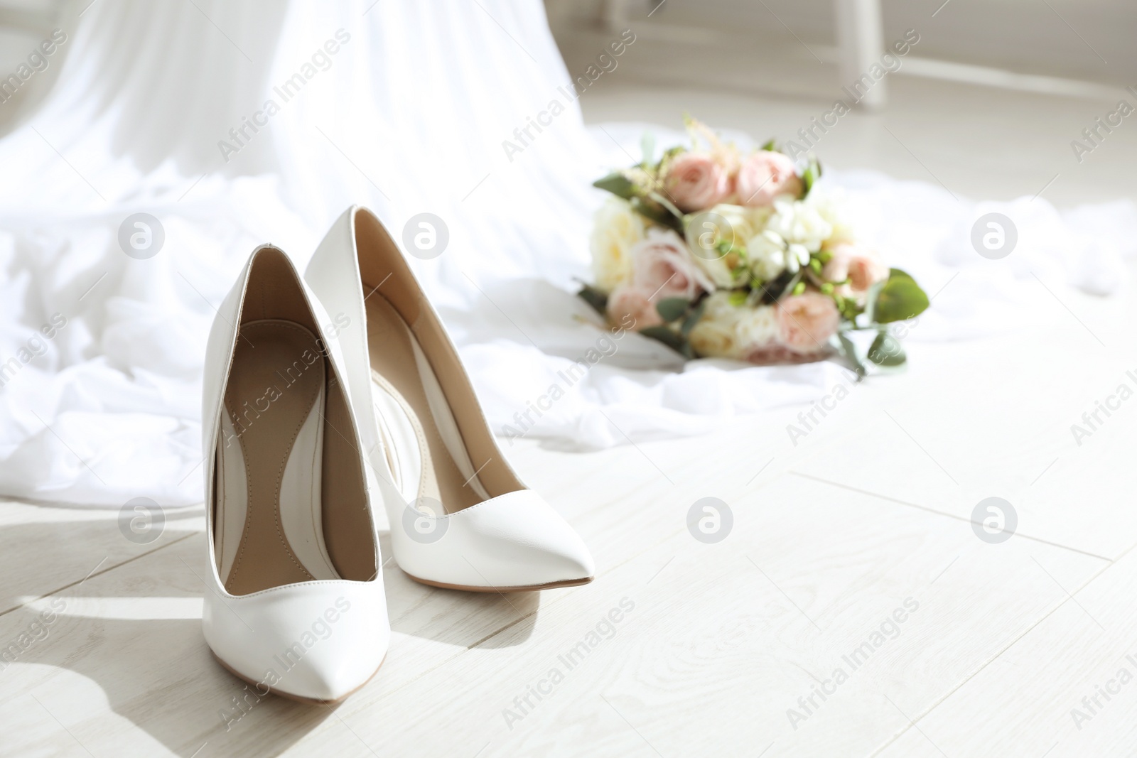 Photo of Pair of wedding high heel shoes on white wooden floor indoors