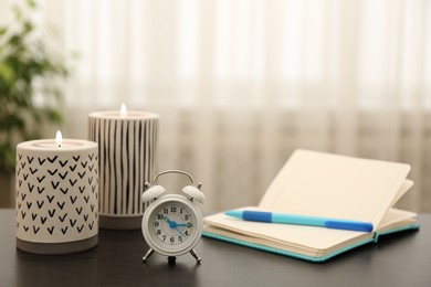 Notebook, alarm clock and burning candles on table indoors