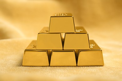Stack of shiny gold bars on yellow fabric, closeup