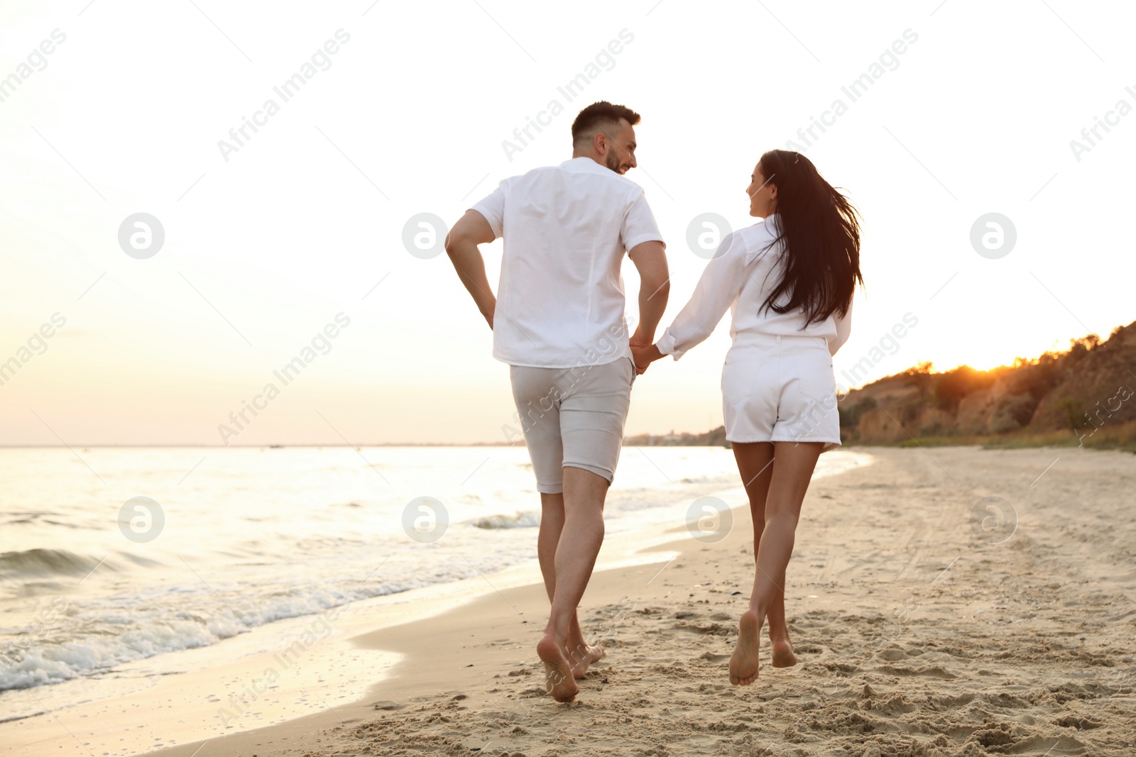 Photo of Lovely couple running together on beach at sunset, back view