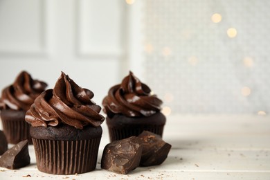 Delicious chocolate cupcakes with cream on white wooden table against blurred lights. Space for text