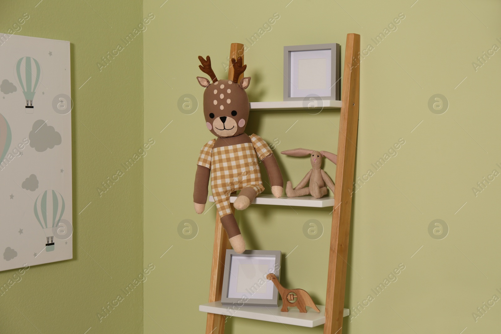 Photo of Wooden decorative ladder with toys and frames near green wall. Interior design