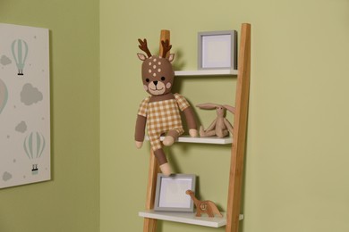 Photo of Wooden decorative ladder with toys and frames near green wall. Interior design