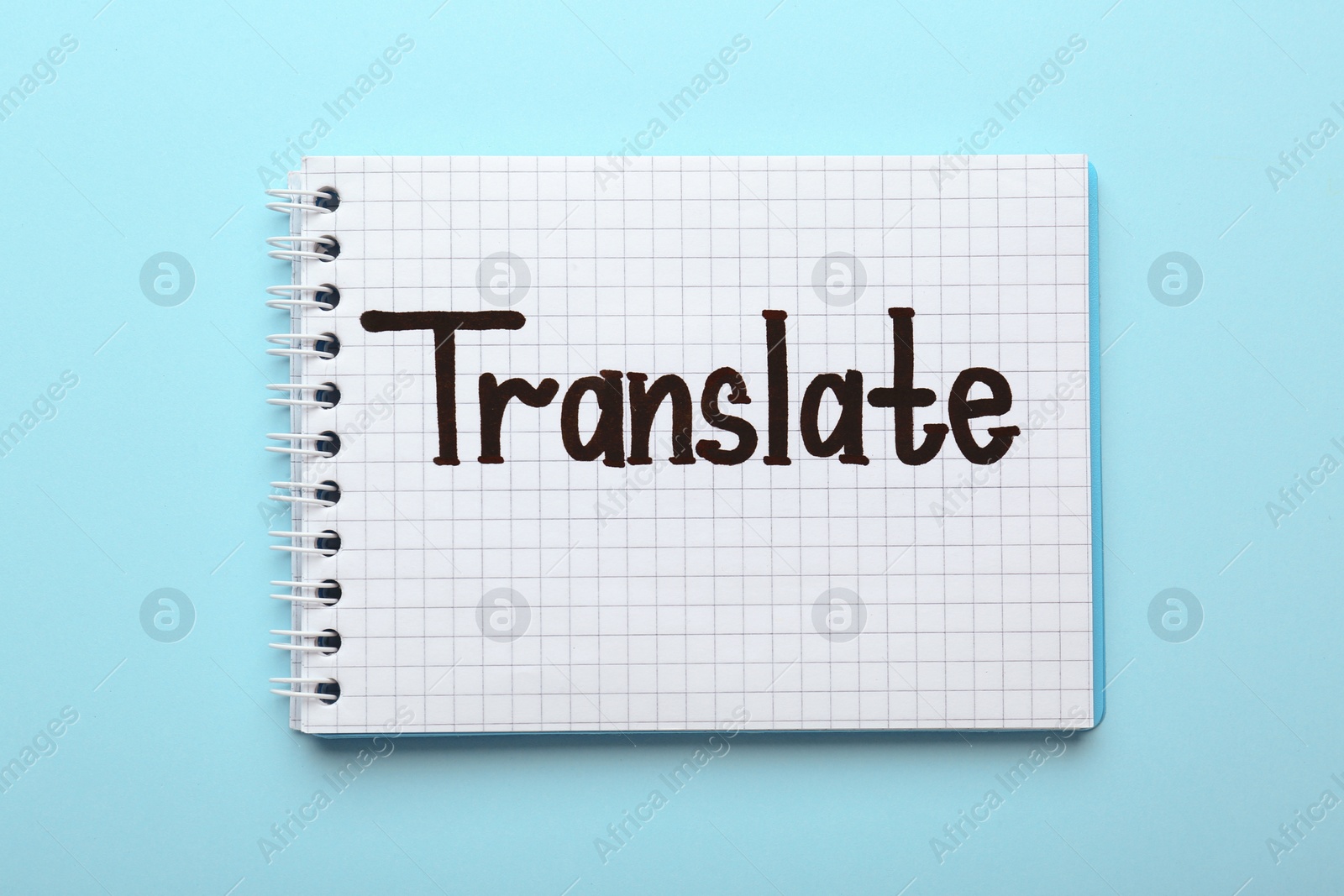 Photo of Notebook with written word Translate on light blue background, top view