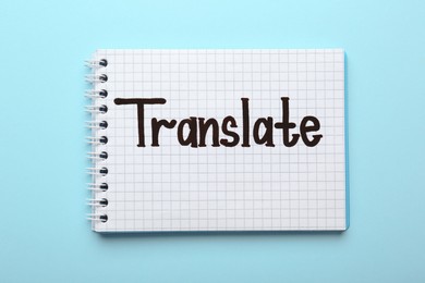 Photo of Notebook with written word Translate on light blue background, top view