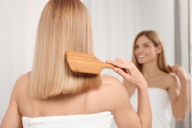 Woman brushing her hair near mirror in room, back view