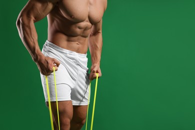 Photo of Muscular man exercising with elastic resistance band on green background, closeup. Space for text