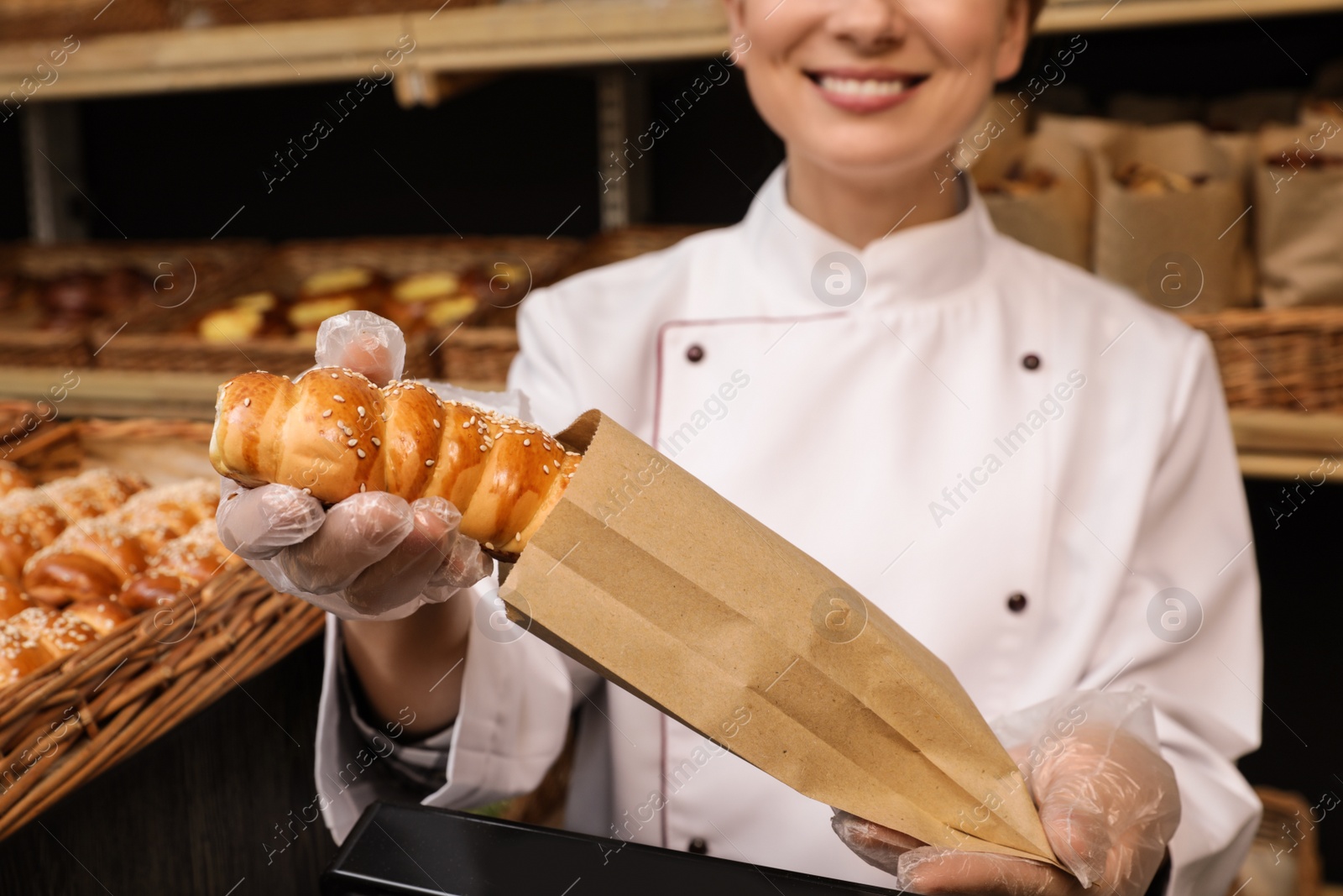 Photo of Baker putting fresh bun into paper bag, closeup