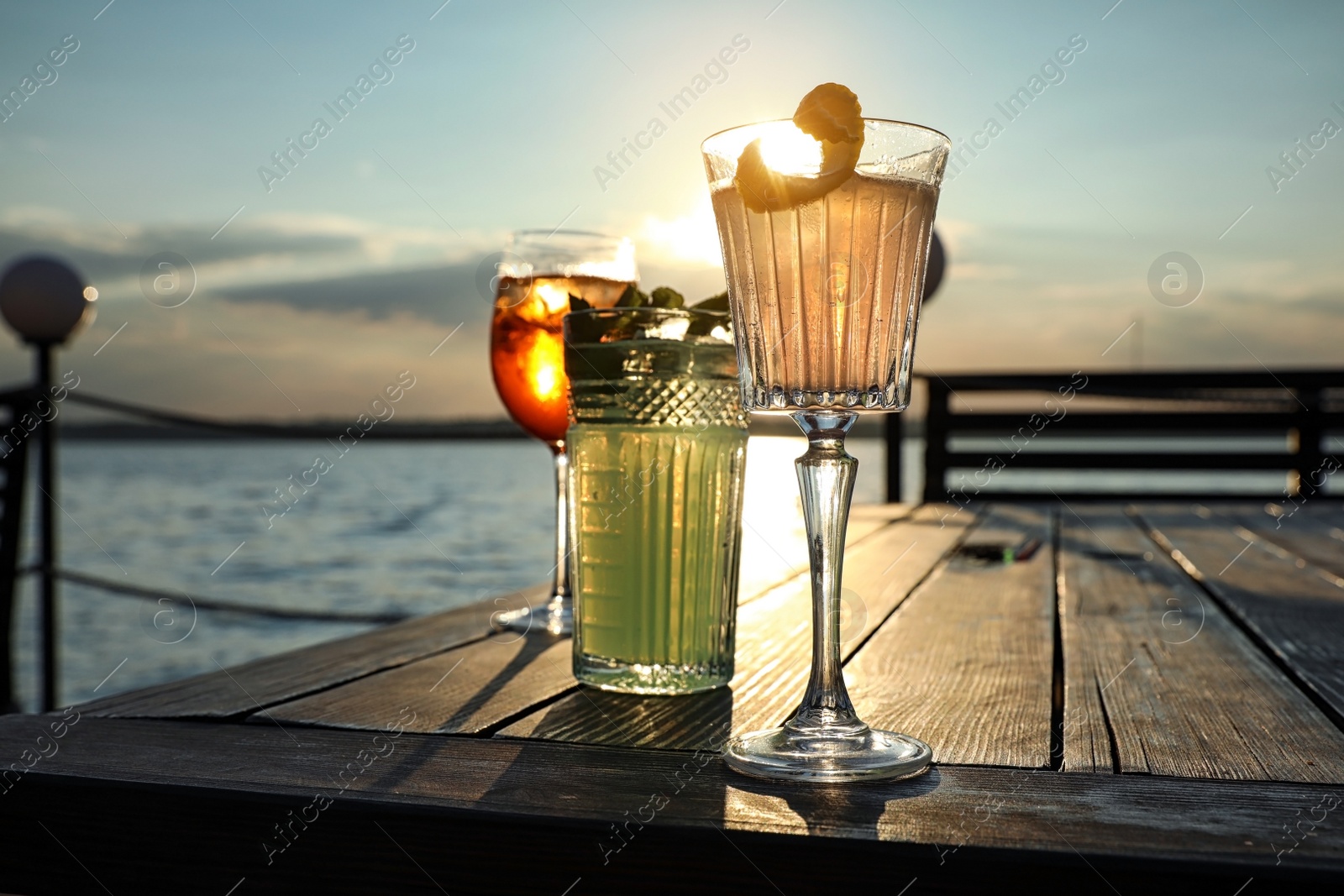 Photo of Glasses of fresh summer cocktails on wooden table outdoors at sunset