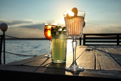 Photo of Glasses of fresh summer cocktails on wooden table outdoors at sunset