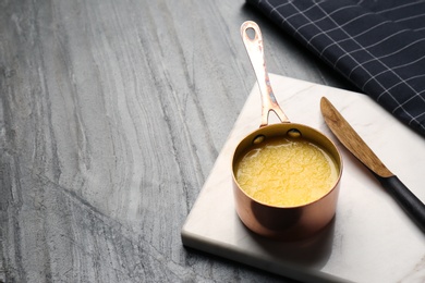 Photo of Stone board with saucepan of clarified butter and knife on table. Space for text