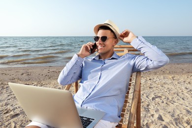 Photo of Happy man with laptop talking by mobile phone on beach. Business trip