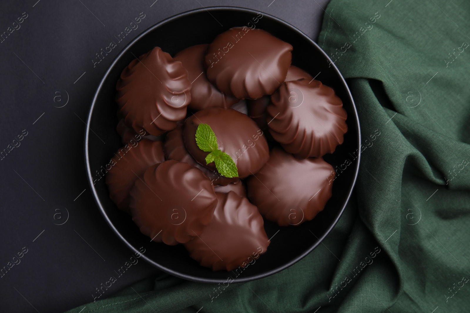 Photo of Delicious chocolate covered zephyrs with mint on black table, top view