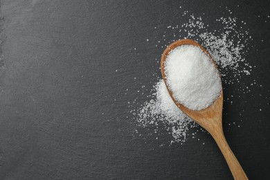 Spoon with granulated sugar on black table, top view. Space for text