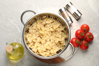 Cooked pasta in metal colander, spices, oil and tomatoes on grey marble table, flat lay