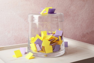 Photo of Colorful paper pieces for lottery and glass container on wooden table