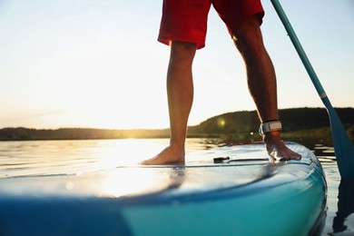 Photo of Man paddle boarding on SUP board in river at sunset, closeup