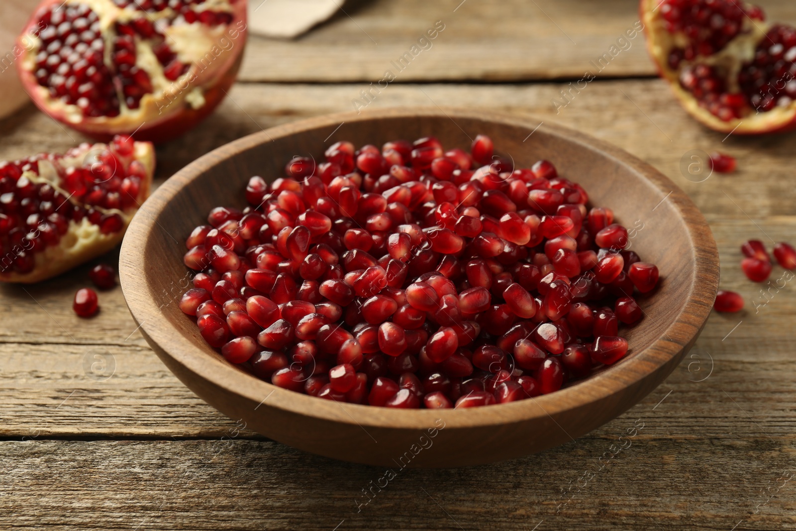 Photo of Ripe juicy pomegranate grains in bowl on wooden table