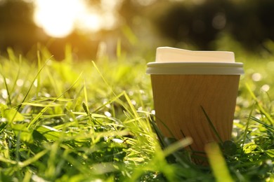 Paper cup on green grass outdoors, closeup with space for text. Coffee to go