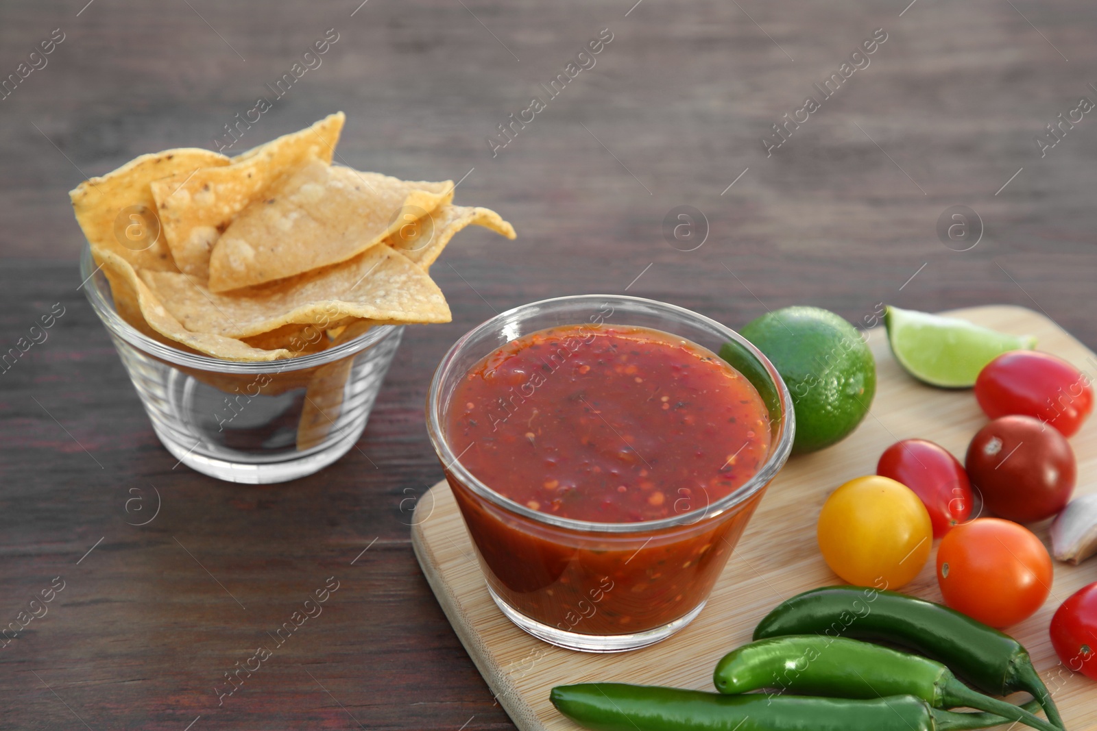 Photo of Tasty salsa sauce with tortilla chips and ingredients on wooden table, closeup