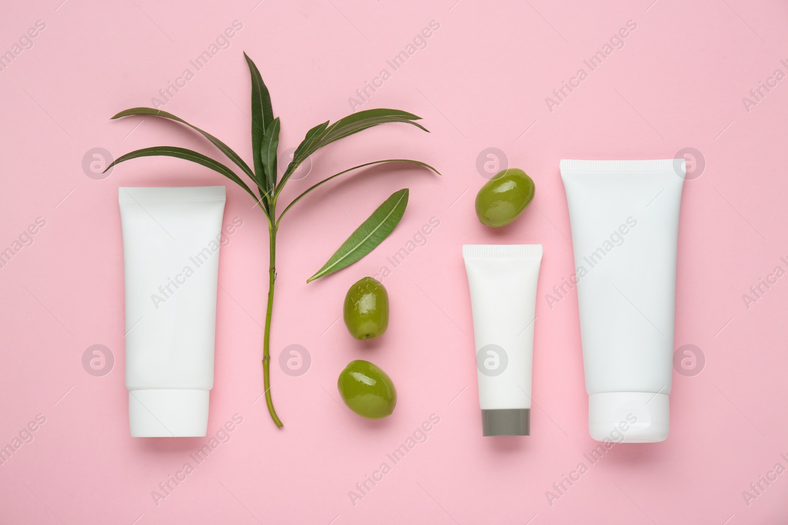 Photo of Tubes of natural cream with olive essential oil on pink background, flat lay