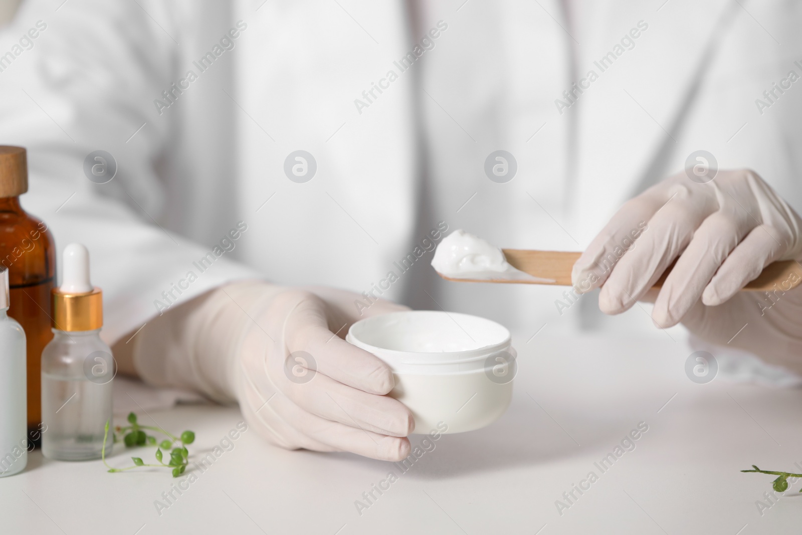 Photo of Dermatologist with jar testing cosmetic product at white table, selective focus