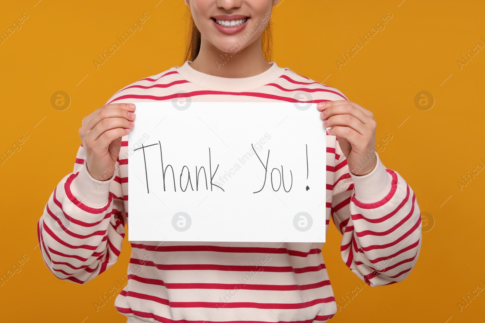 Photo of Woman holding card with phrase Thank You on orange background, closeup