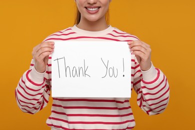 Photo of Woman holding card with phrase Thank You on orange background, closeup