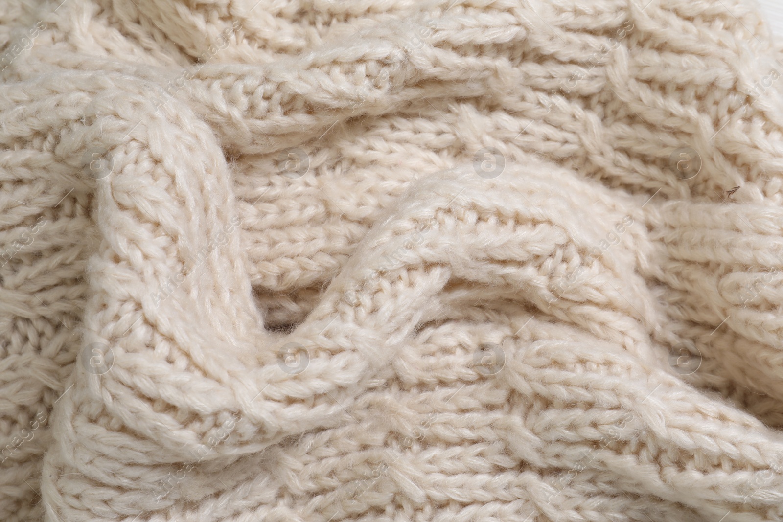 Photo of Beige knitted scarf as background, closeup view