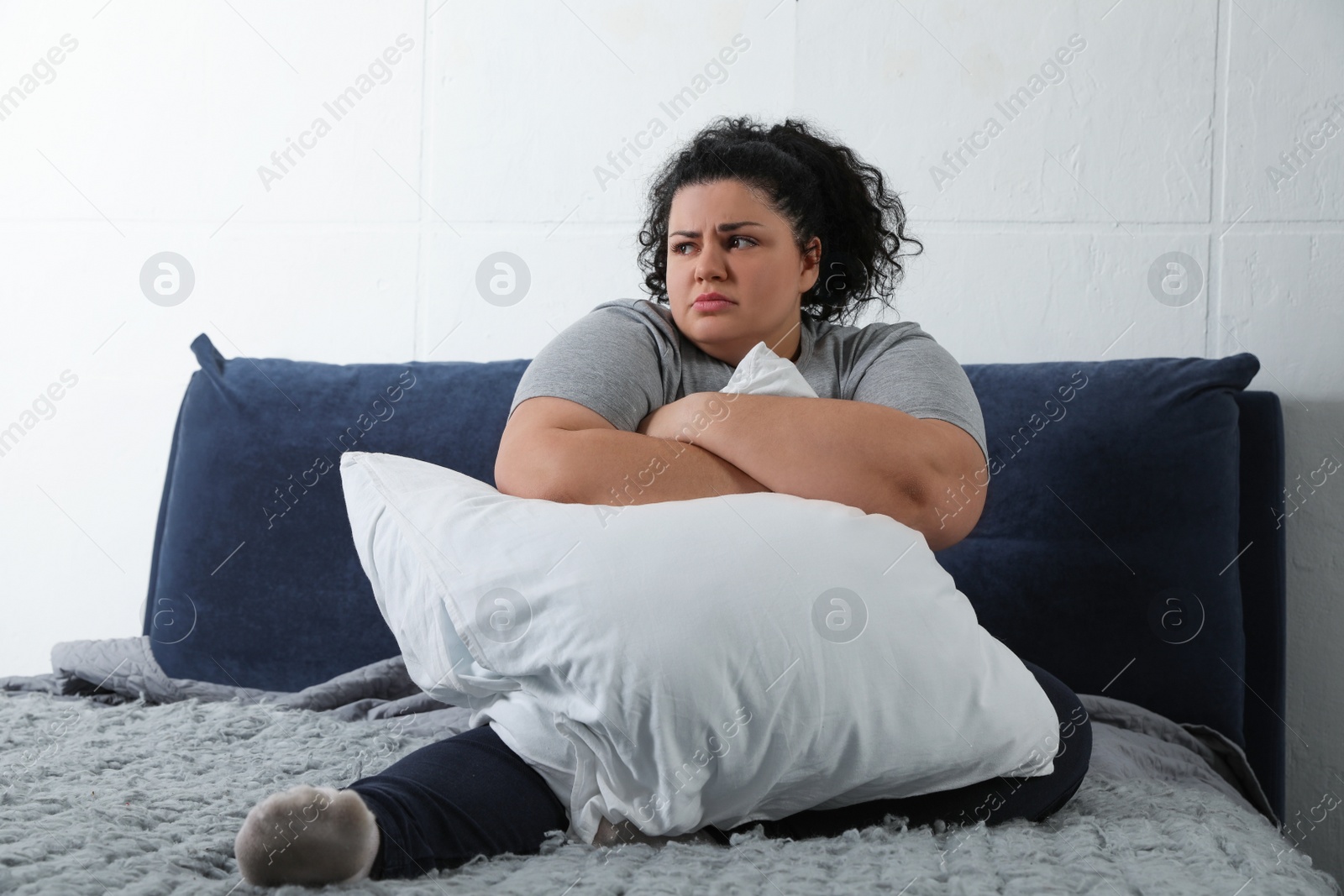 Photo of Depressed overweight woman hugging pillow on bed