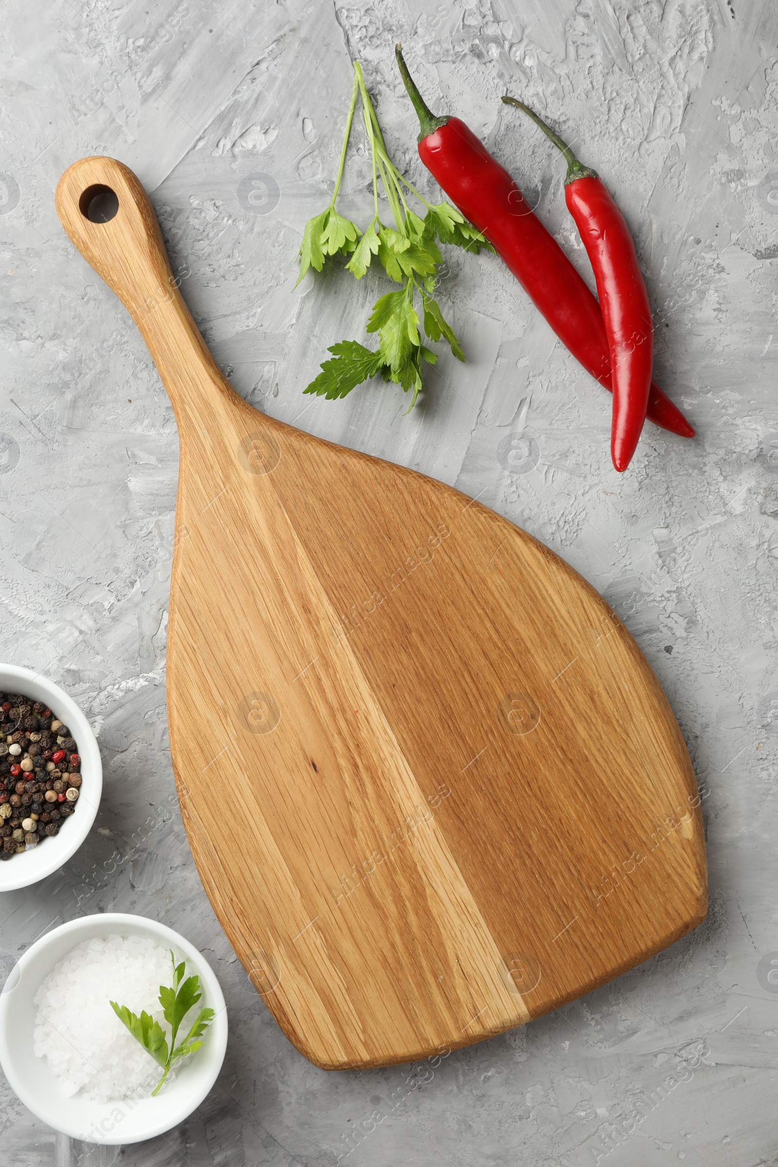 Photo of Cutting board, salt, spices, chili peppers and parsley on grey textured table, flat lay. Space for text