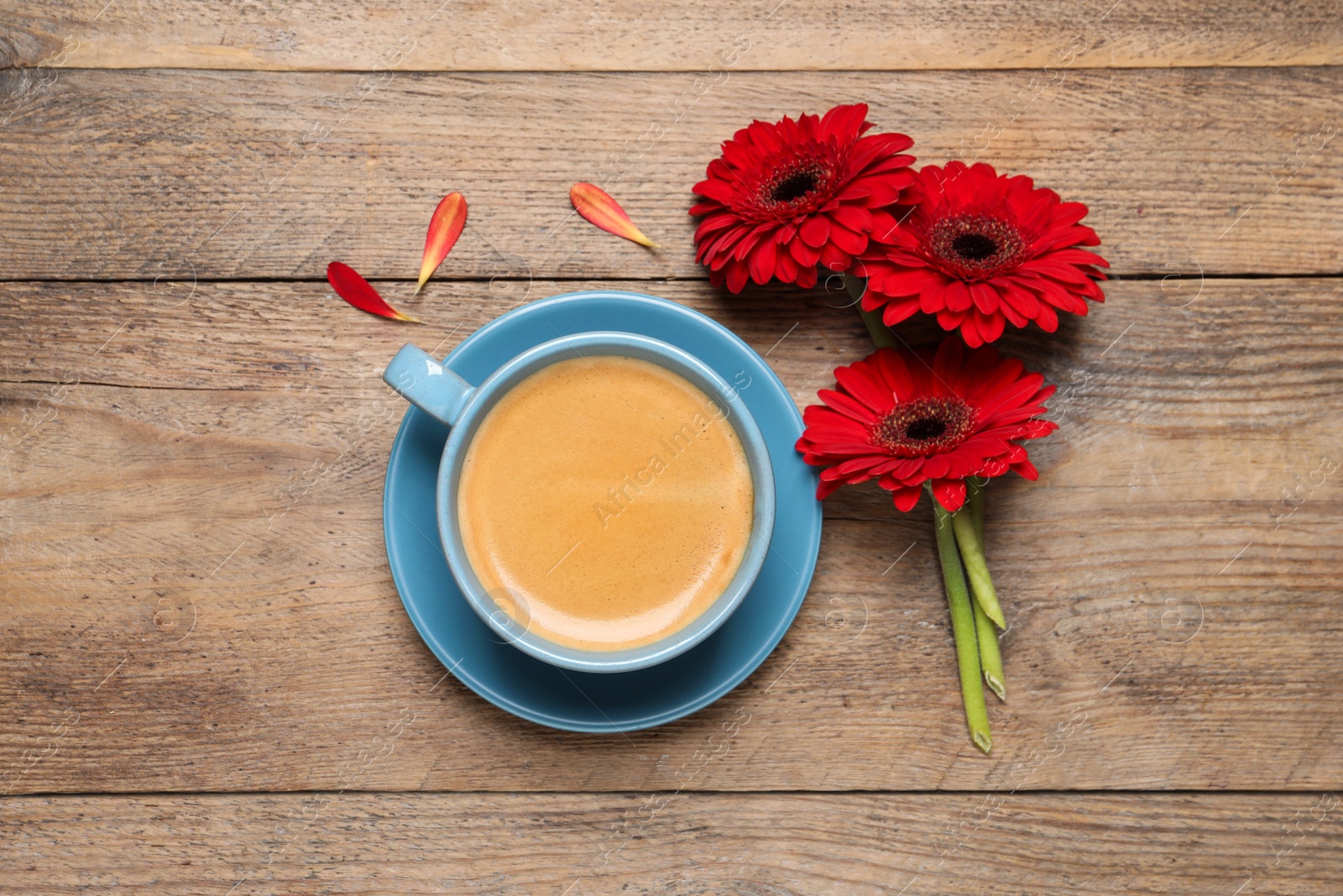 Photo of Cup of coffee and red gerbera flowers on wooden table, flat lay
