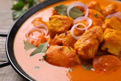 Photo of Delicious chicken curry in pan on wooden table, closeup