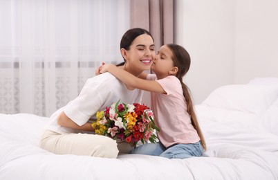 Photo of Happy woman with her daughter and bouquet of lilies on bed at home. Mother's day celebration