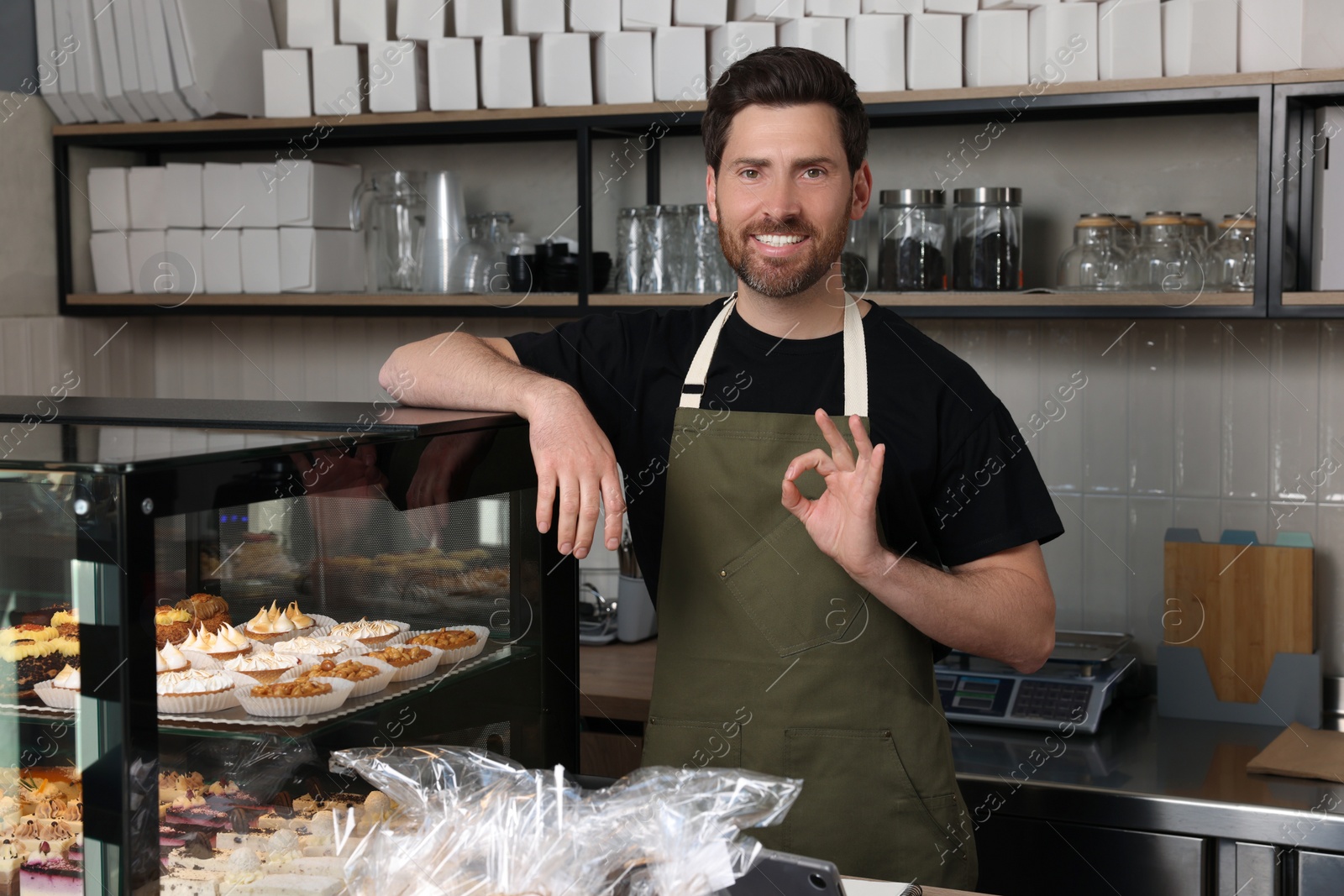 Photo of Happy seller showing OK gesture at cashier desk in bakery shop