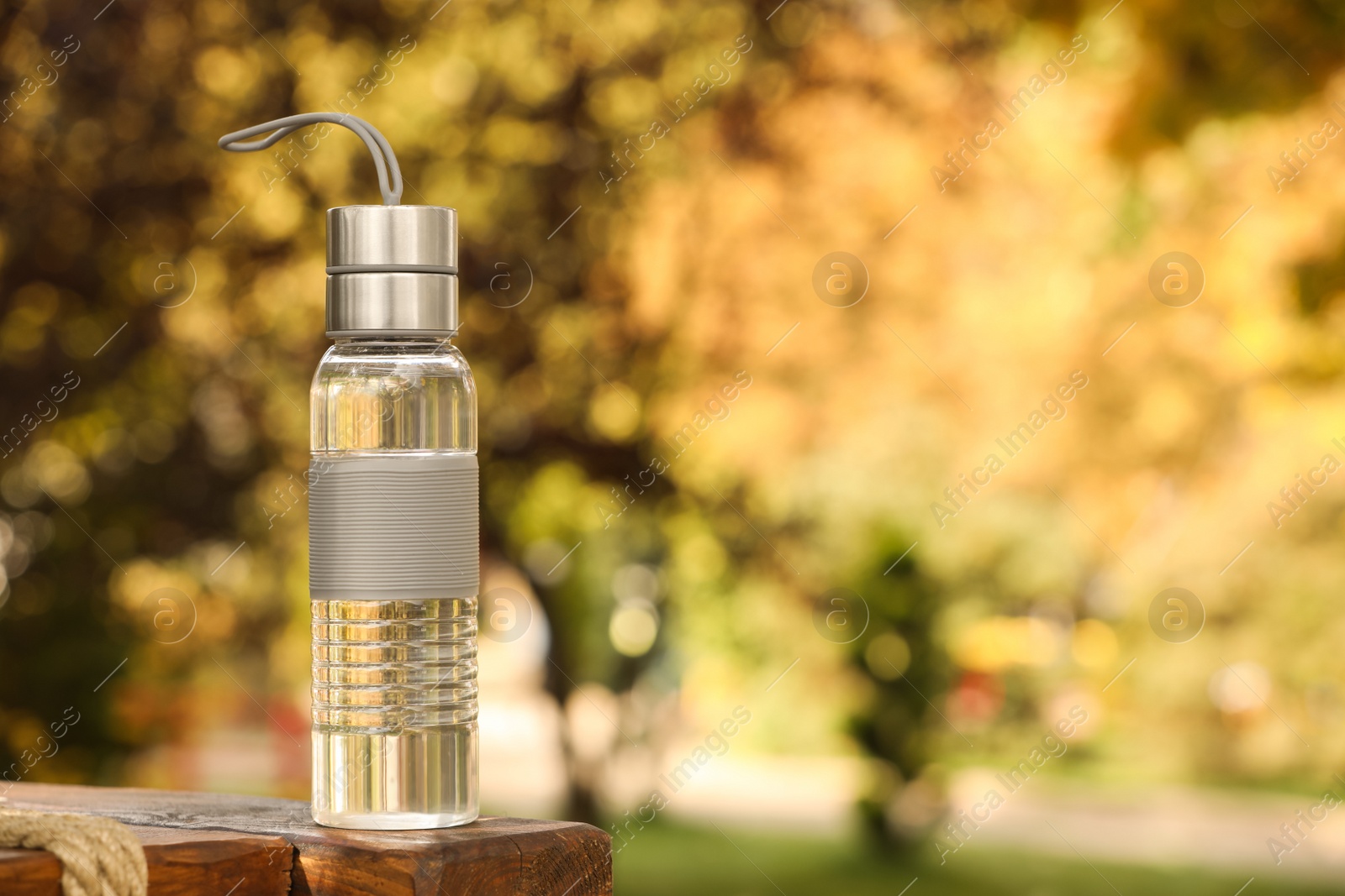 Photo of Sport bottle of water on wooden bench in park, space for text