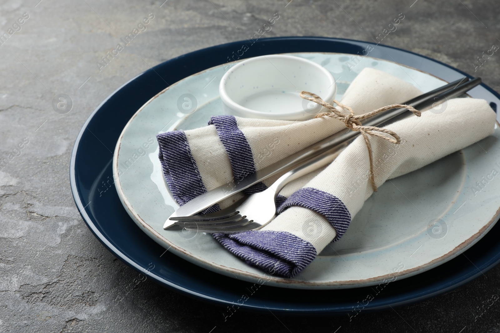 Photo of Stylish setting with cutlery, plates, bowl and napkin on grey textured table, closeup